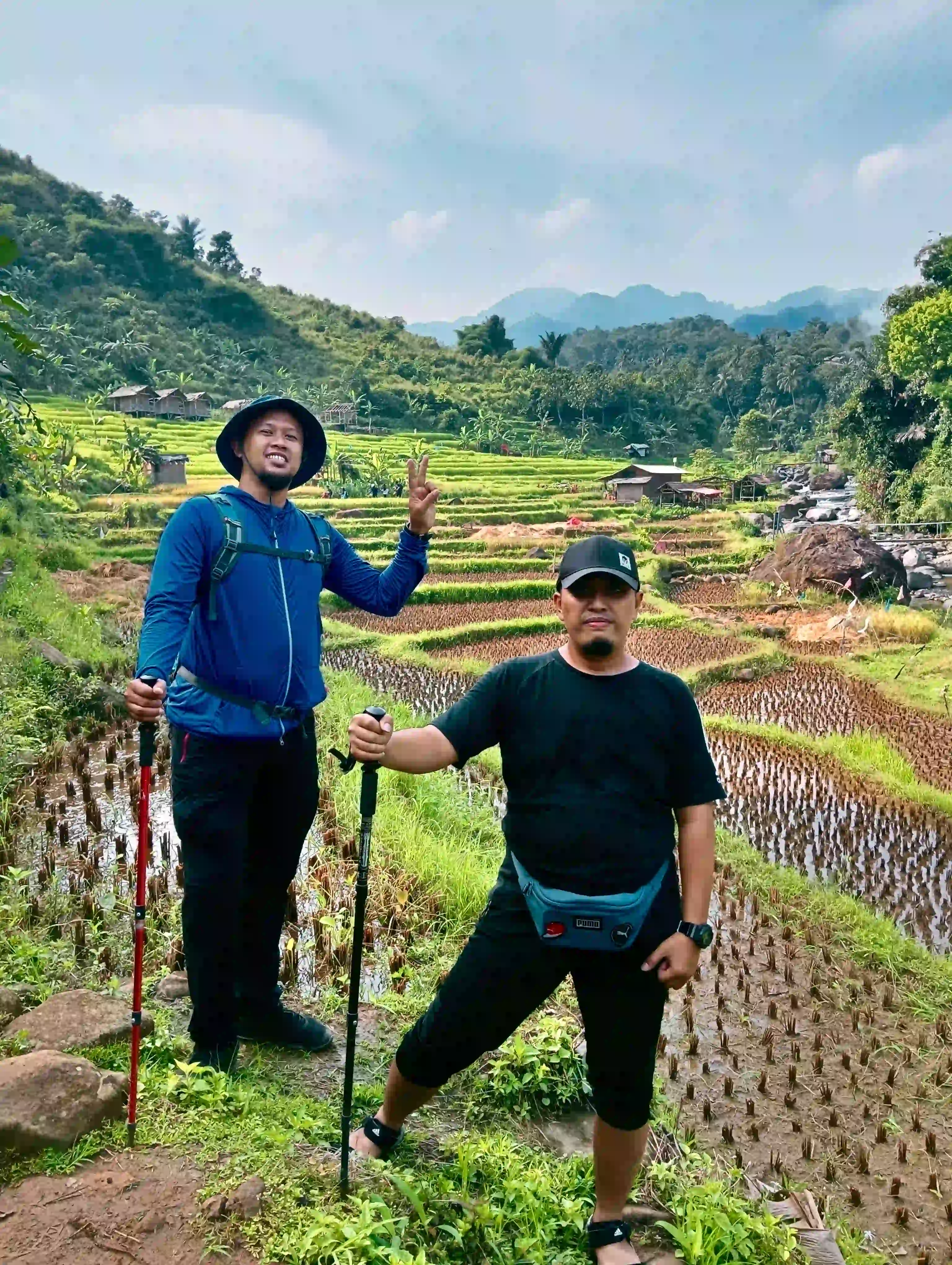 Dua peserta pria berpose di area persawahan bertingkat dengan latar pedesaan.