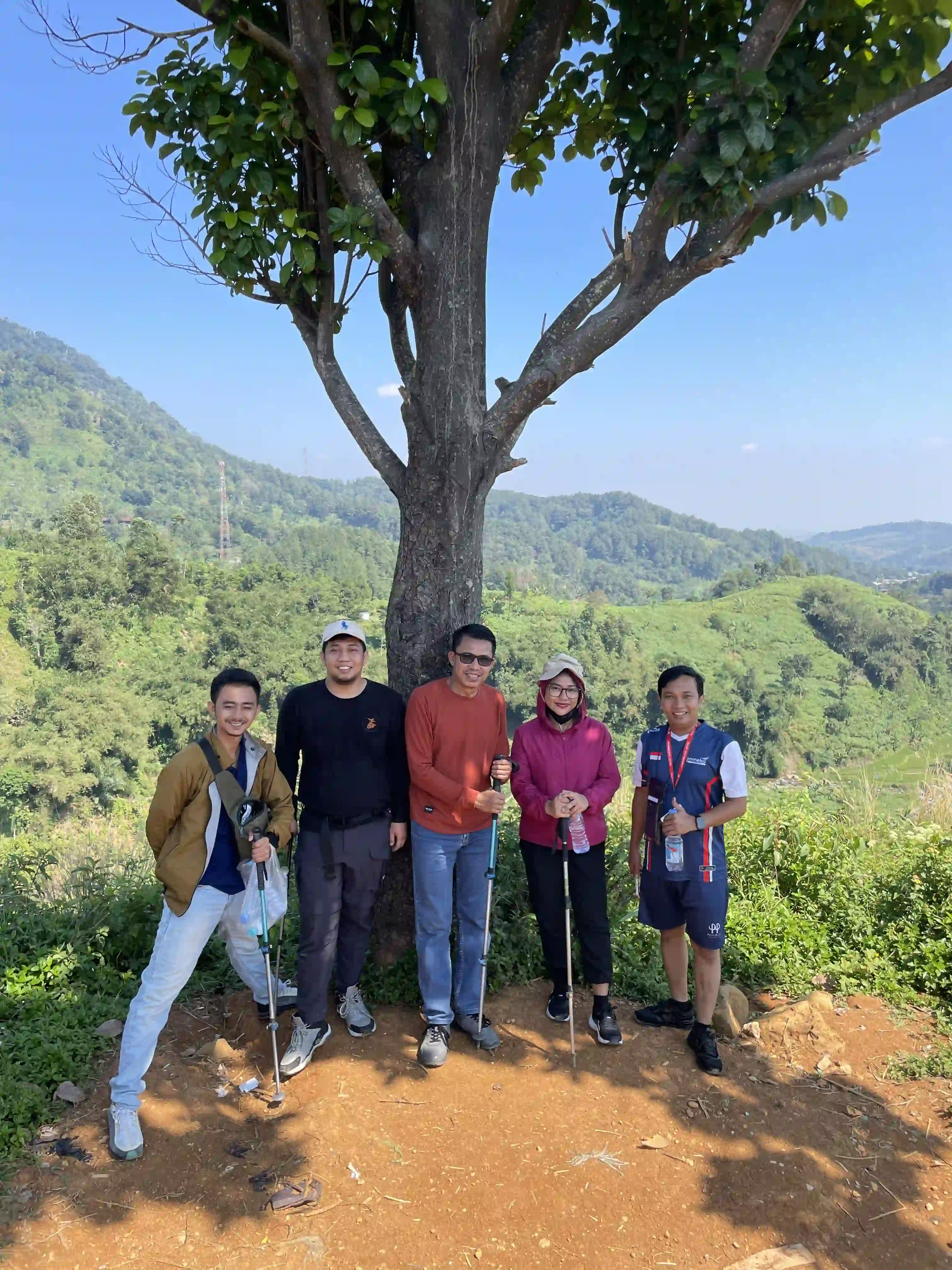 Lima peserta berpose di bawah pohon besar dengan pemandangan lembah hijau yang luas.