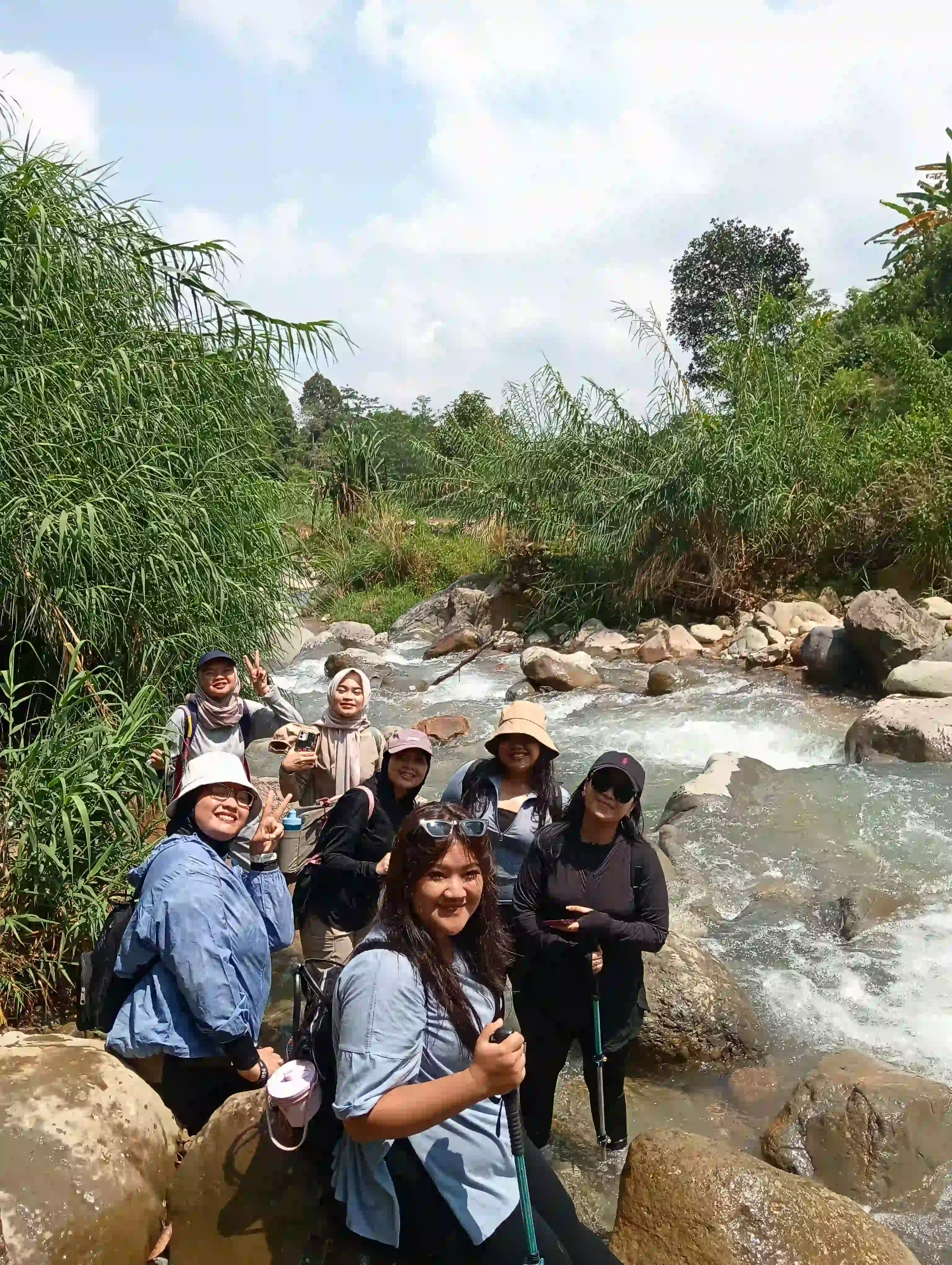 Sekelompok peserta wanita berpose di antara bebatuan besar di pinggir aliran sungai yang deras.