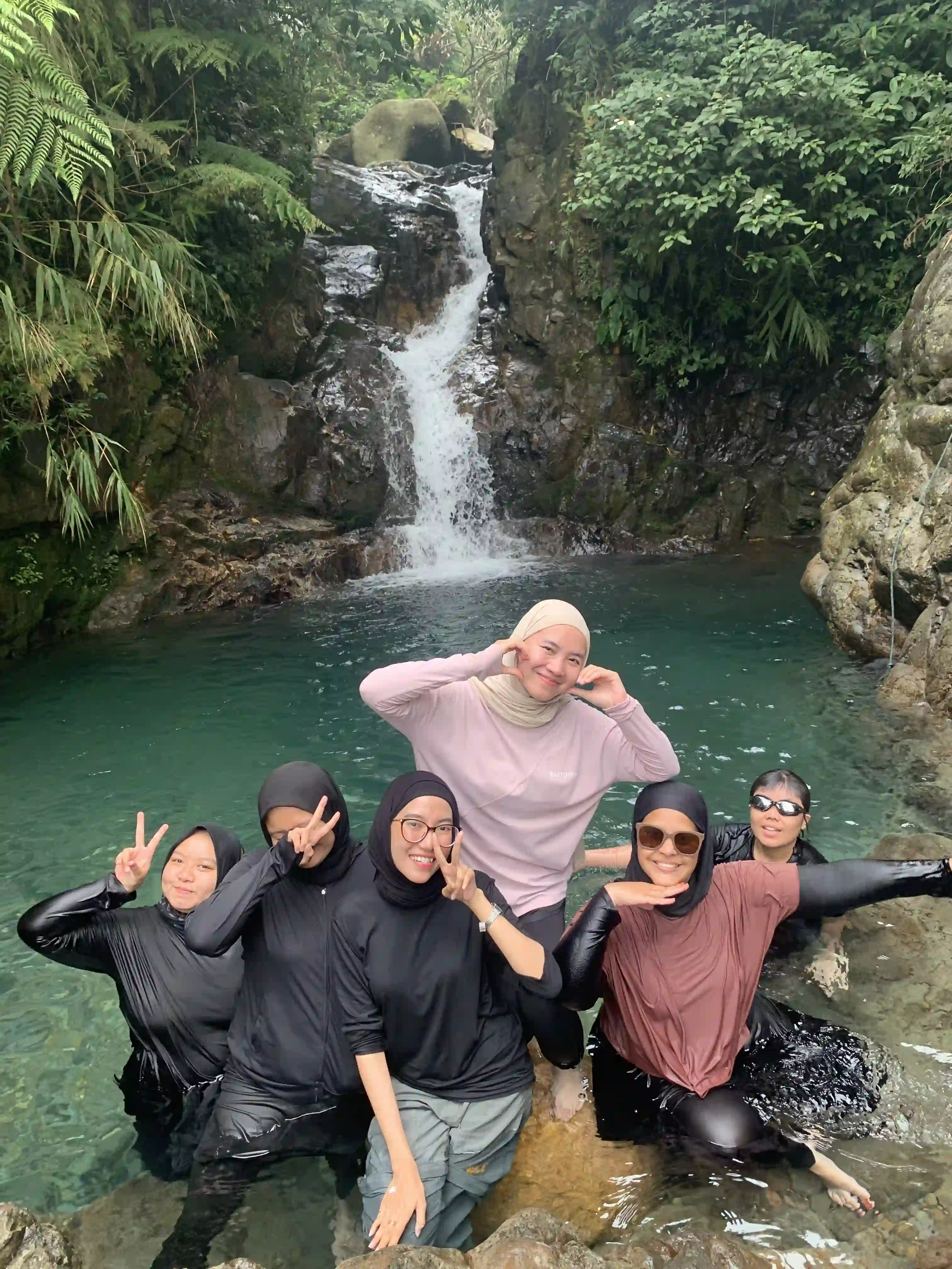 Peserta wanita dengan pakaian pink berpose gembira di depan aliran air terjun yang asri.
