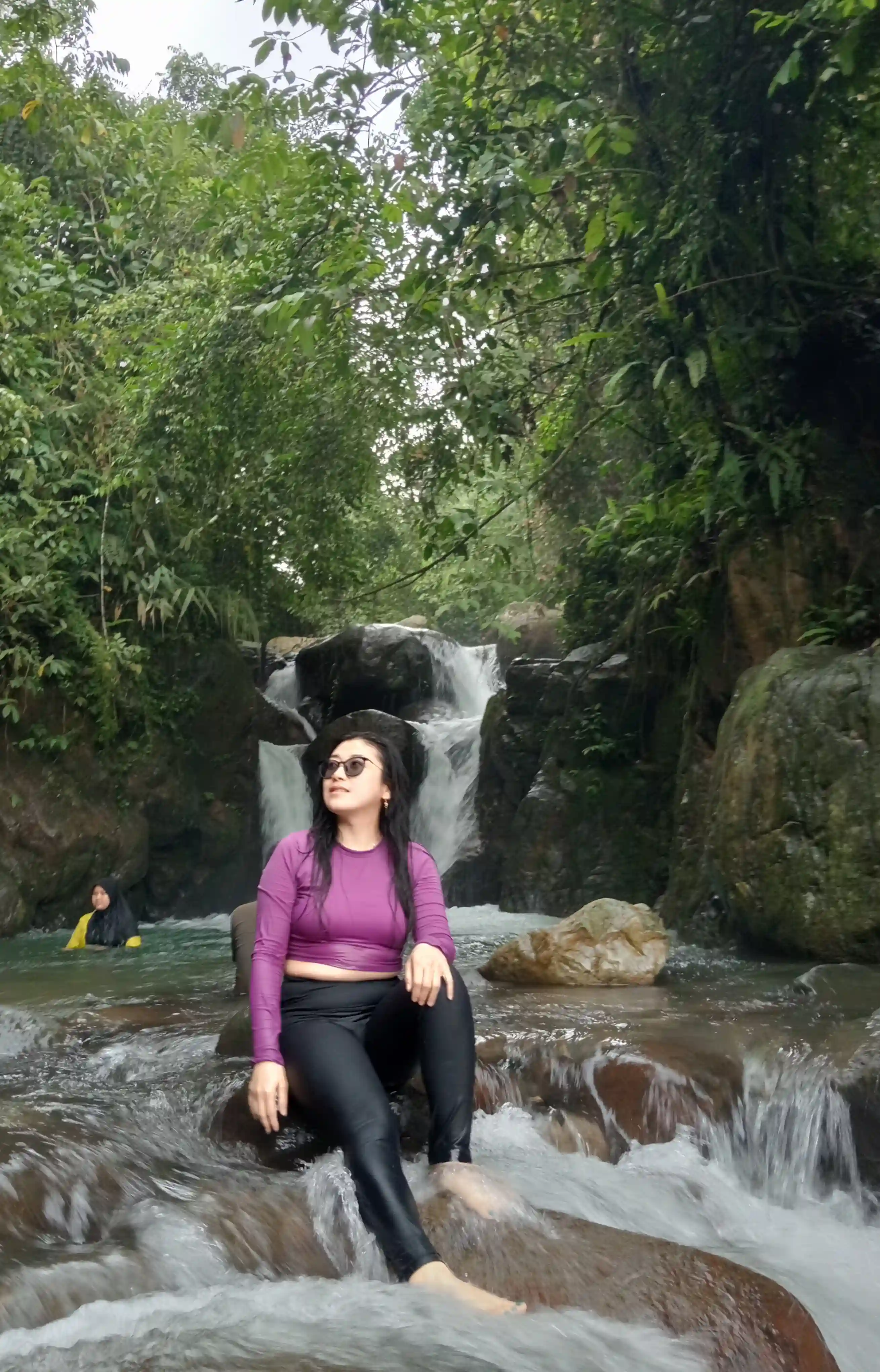 Potret peserta wanita menikmati suasana tenang sambil duduk di atas batu di tengah sungai.