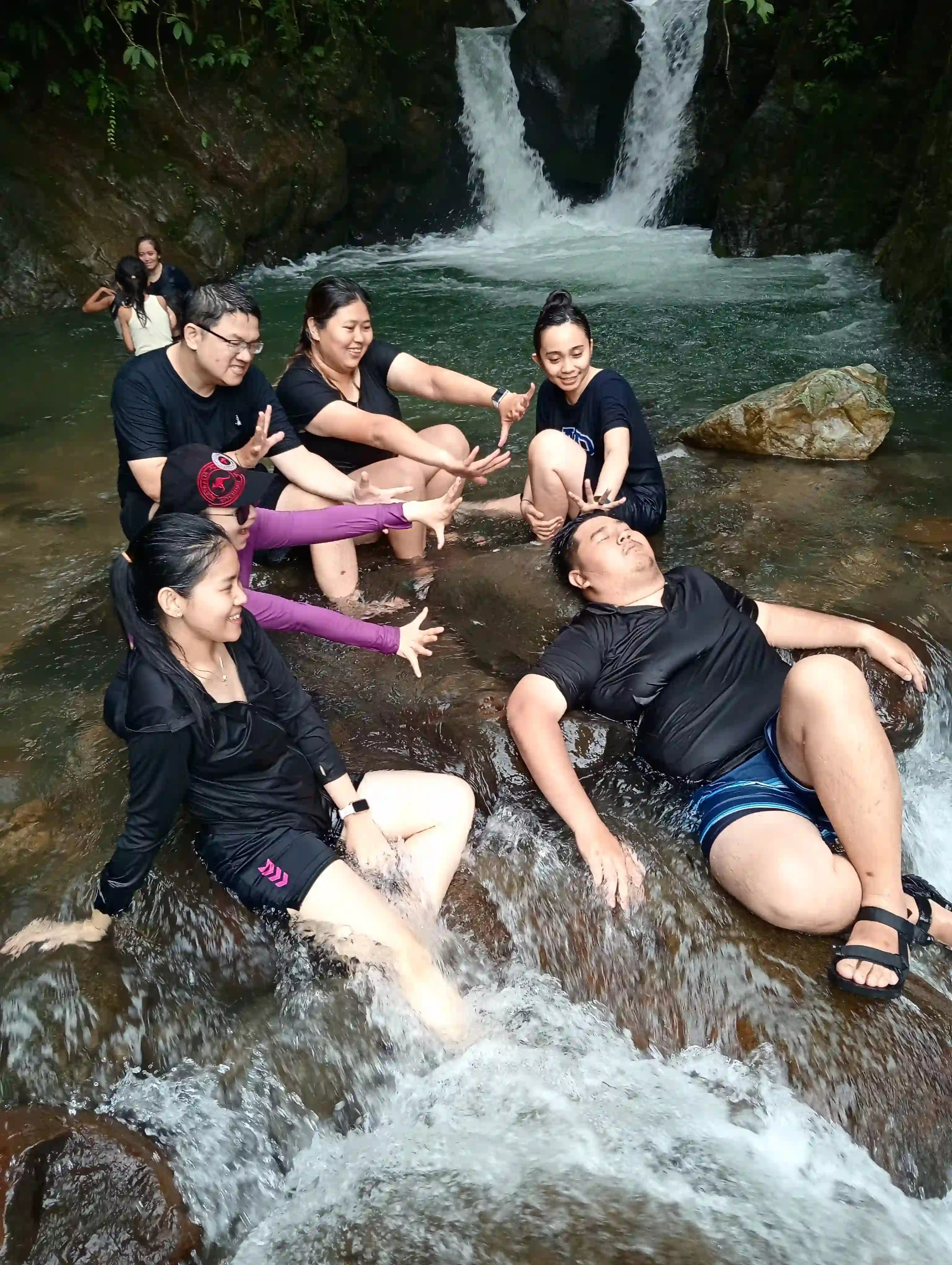 Momen santai dan lucu peserta trekking berpose di antara bebatuan sungai setelah berendam.